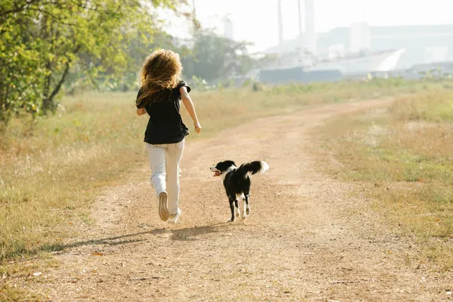 A girl running with her dog along a dirt path in a park