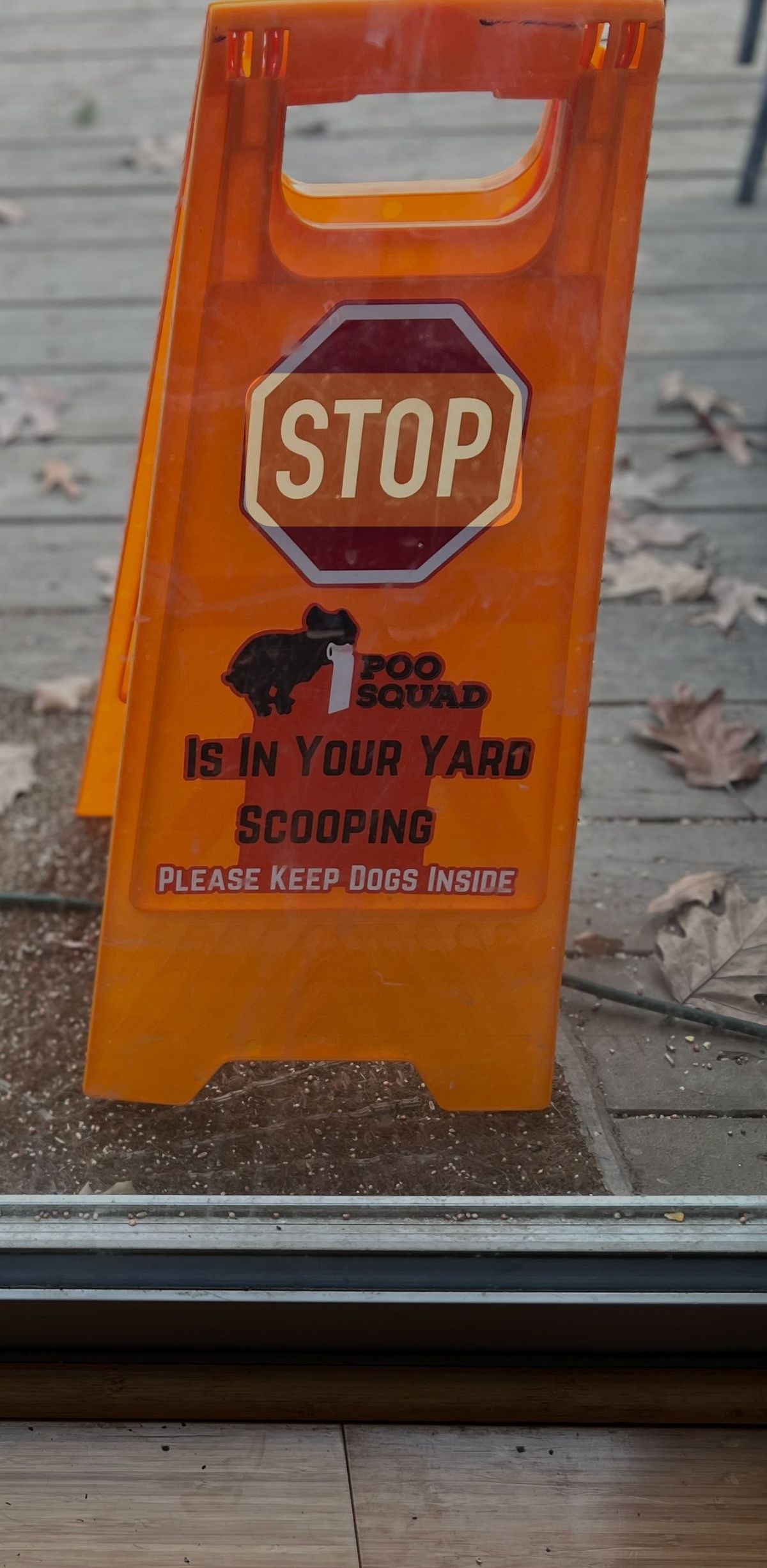 Orange Poo Squad sign on a patio asking owners to keep dogs inside while the yard is scooped