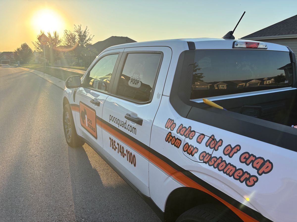 White Poo Squad truck with orange logo and funny slogan parked on a residential street at sunrise